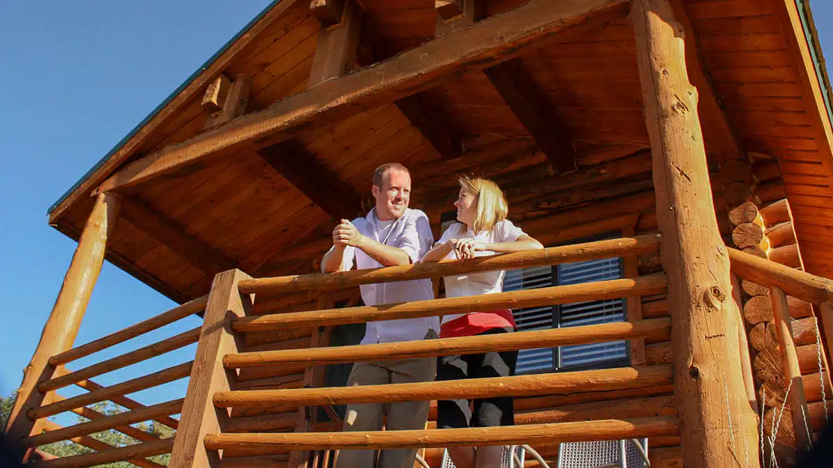 A couple stands on the balcony of a log cabin, enjoying the outdoors.