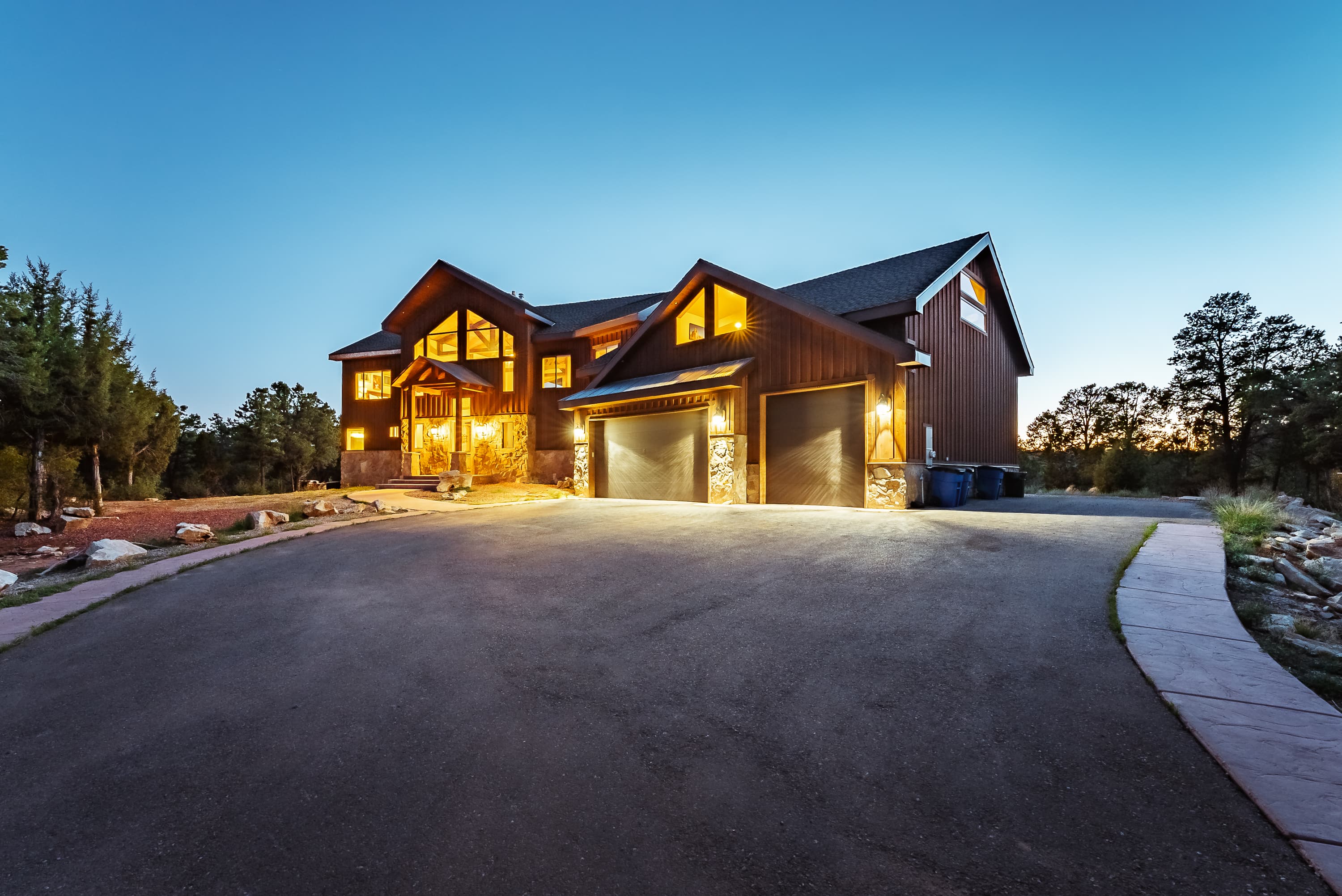 A modern two-story house with warm lighting set against a twilight sky.