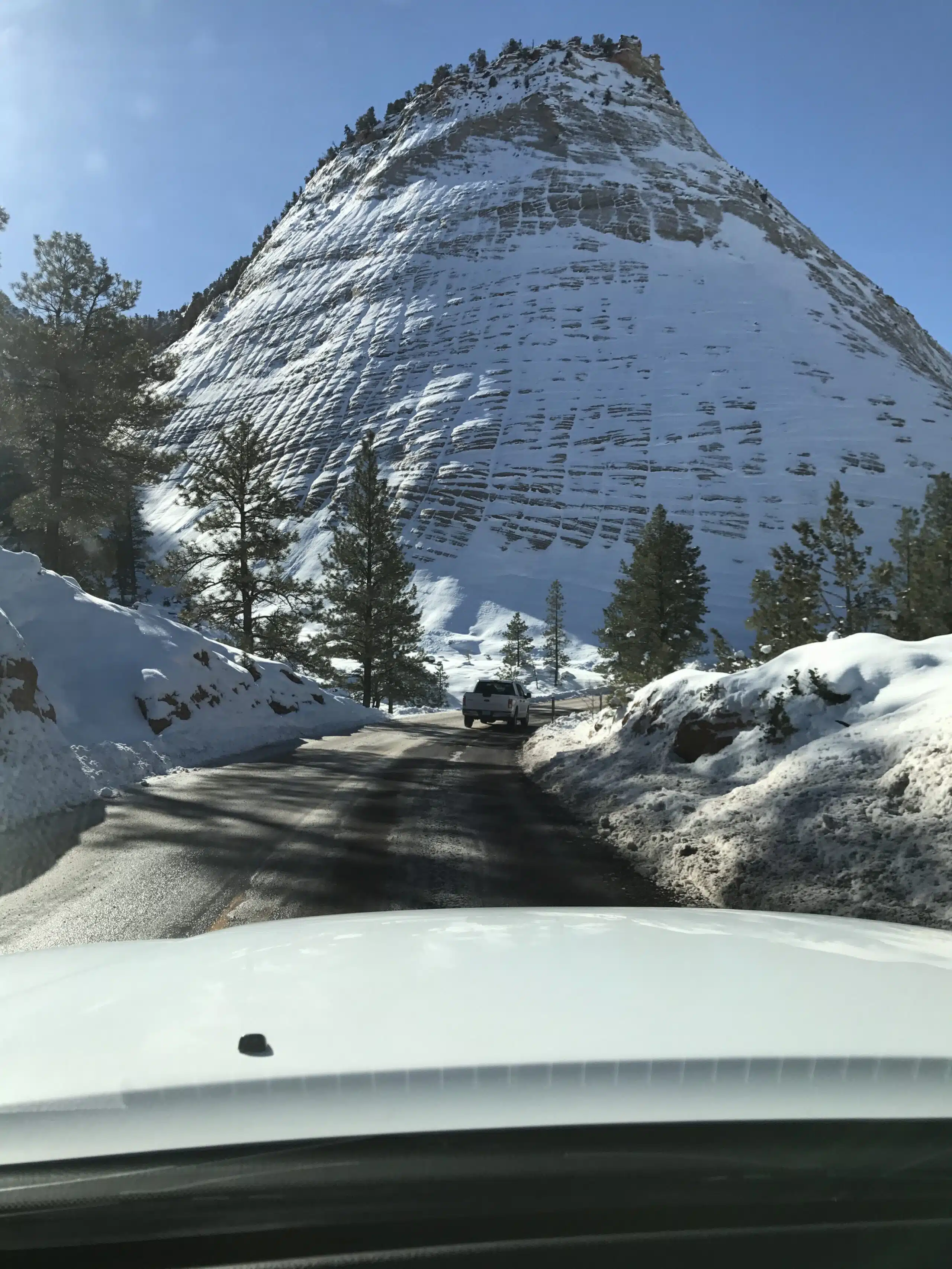 A snow-covered mountain looms over a winding road with a vehicle ahead.