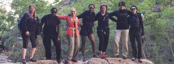A group of seven women stands together on a rock formation in a natural setting.