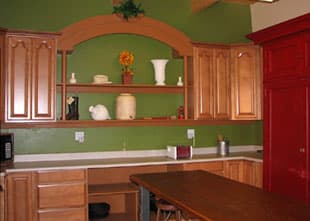 A kitchen with wooden cabinets, green walls, and a countertop decorated with ceramic vases and a fruit arrangement.