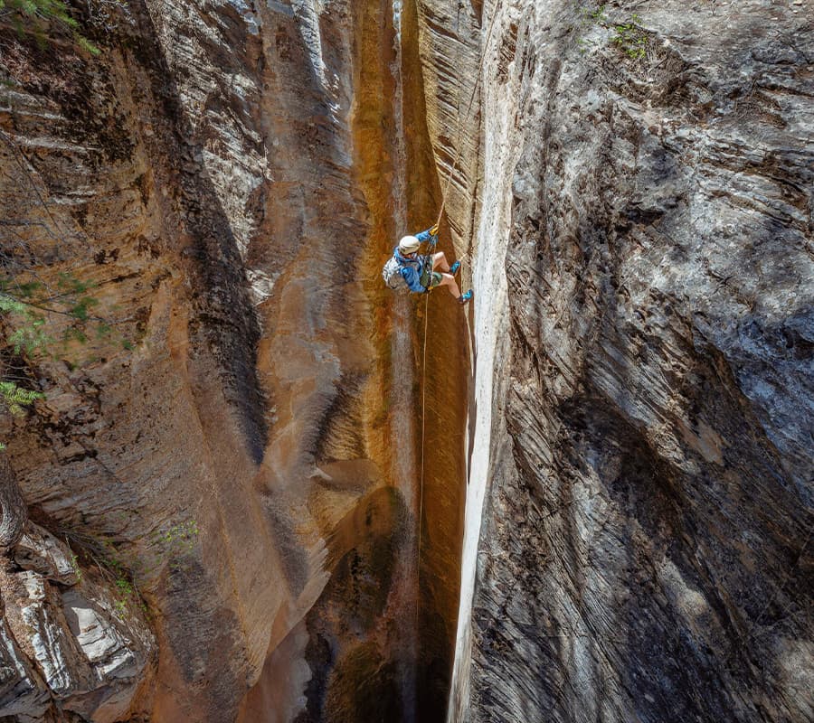 A climber rappels down a steep rock face in a narrow canyon.
