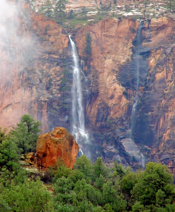 A waterfall cascades down a rocky cliff surrounded by trees.