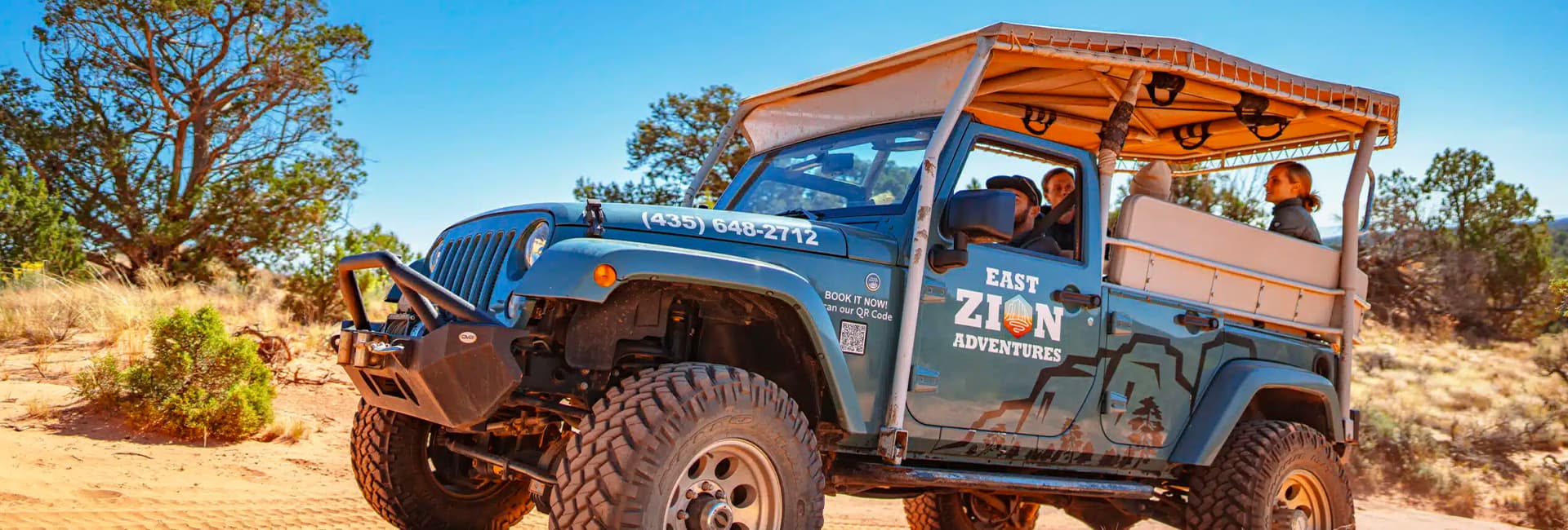A rugged off-road Jeep marked "East Zion Adventures" parked on a sandy trail with travelers inside.
