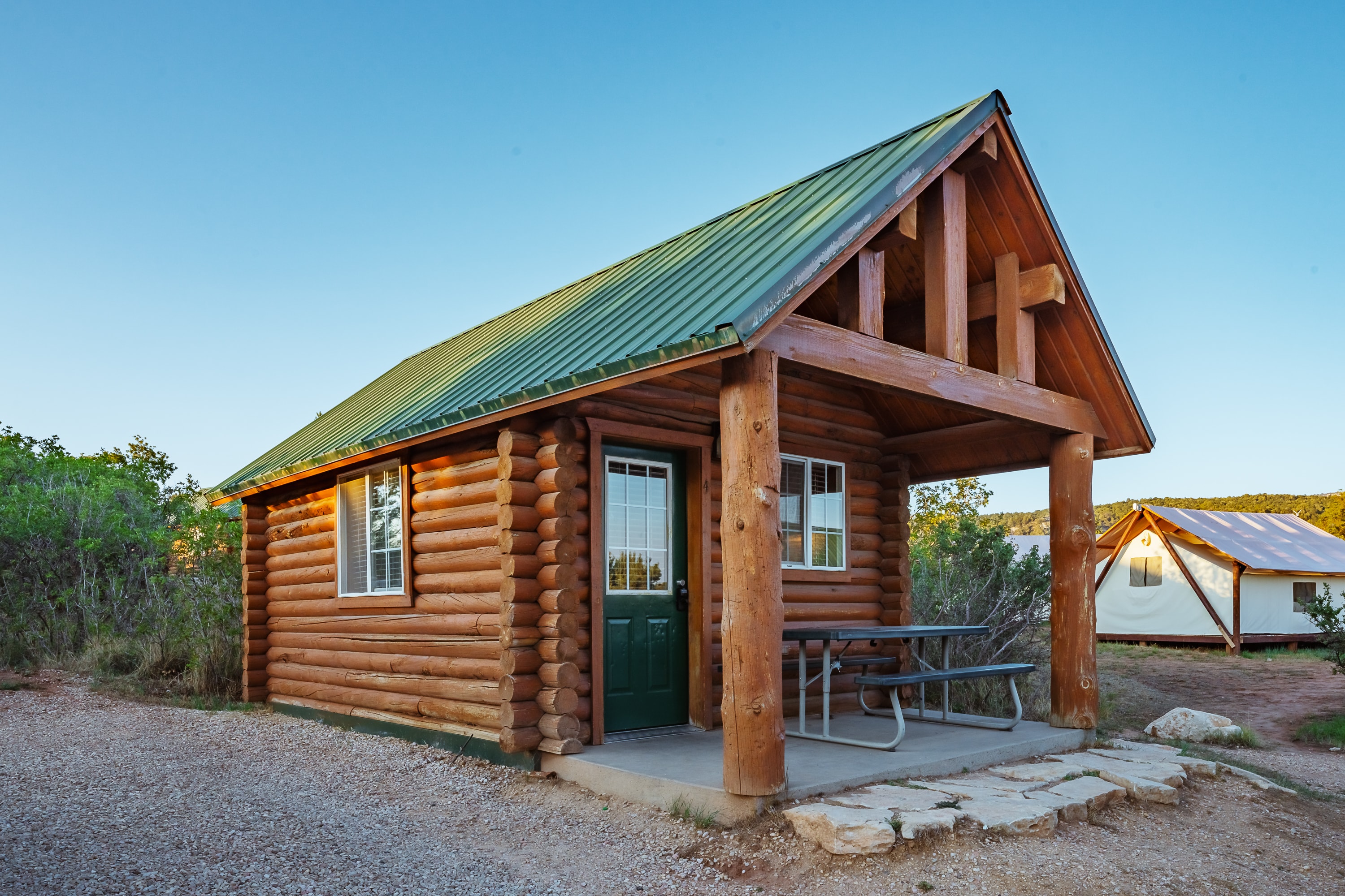 A small wooden cabin with a green metal roof and a picnic table in front.