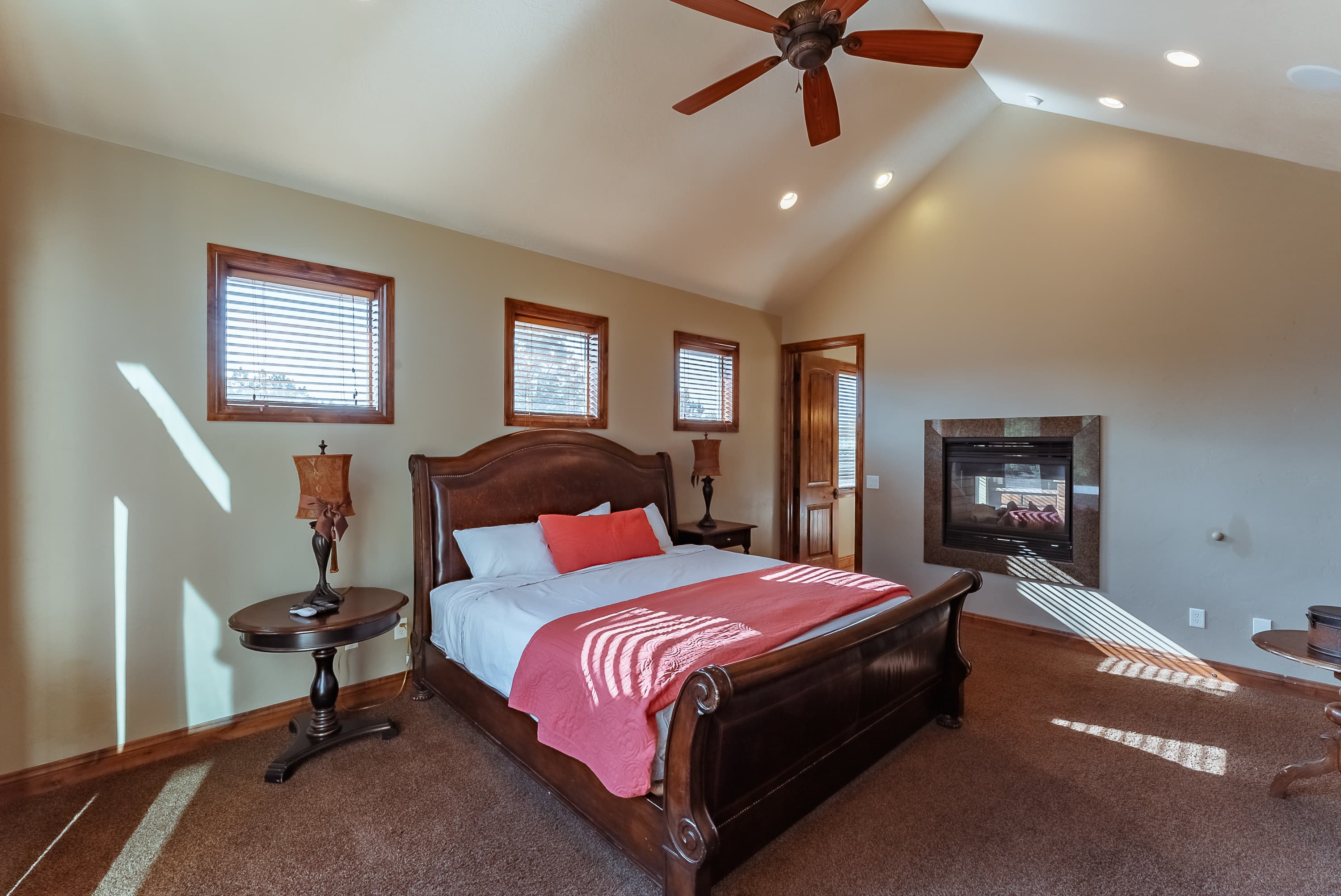A well-lit bedroom featuring a wooden bed, red accents, and a cozy fireplace.