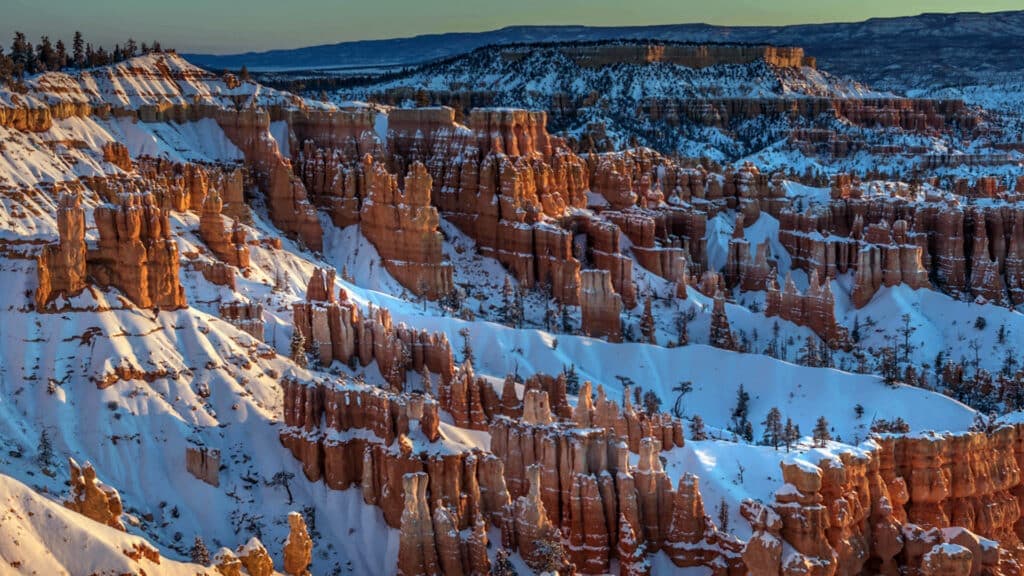 Snow-covered rock formations in a canyon landscape at sunset.