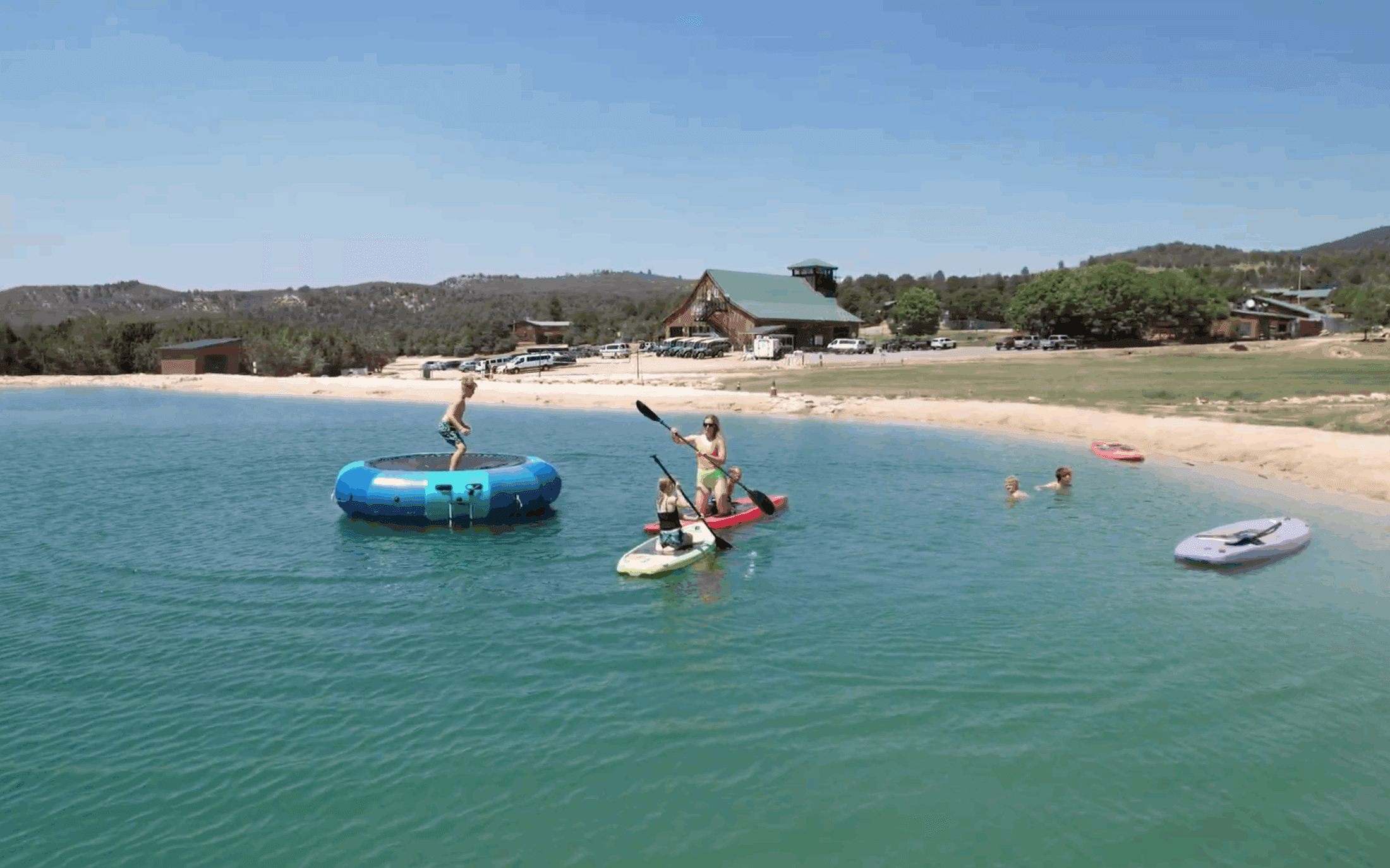 Children enjoying water activities at a lakeside beach on a sunny day.