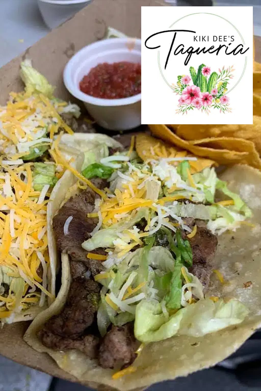 Two tacos filled with meat, lettuce, and cheese, accompanied by salsa and tortilla chips.