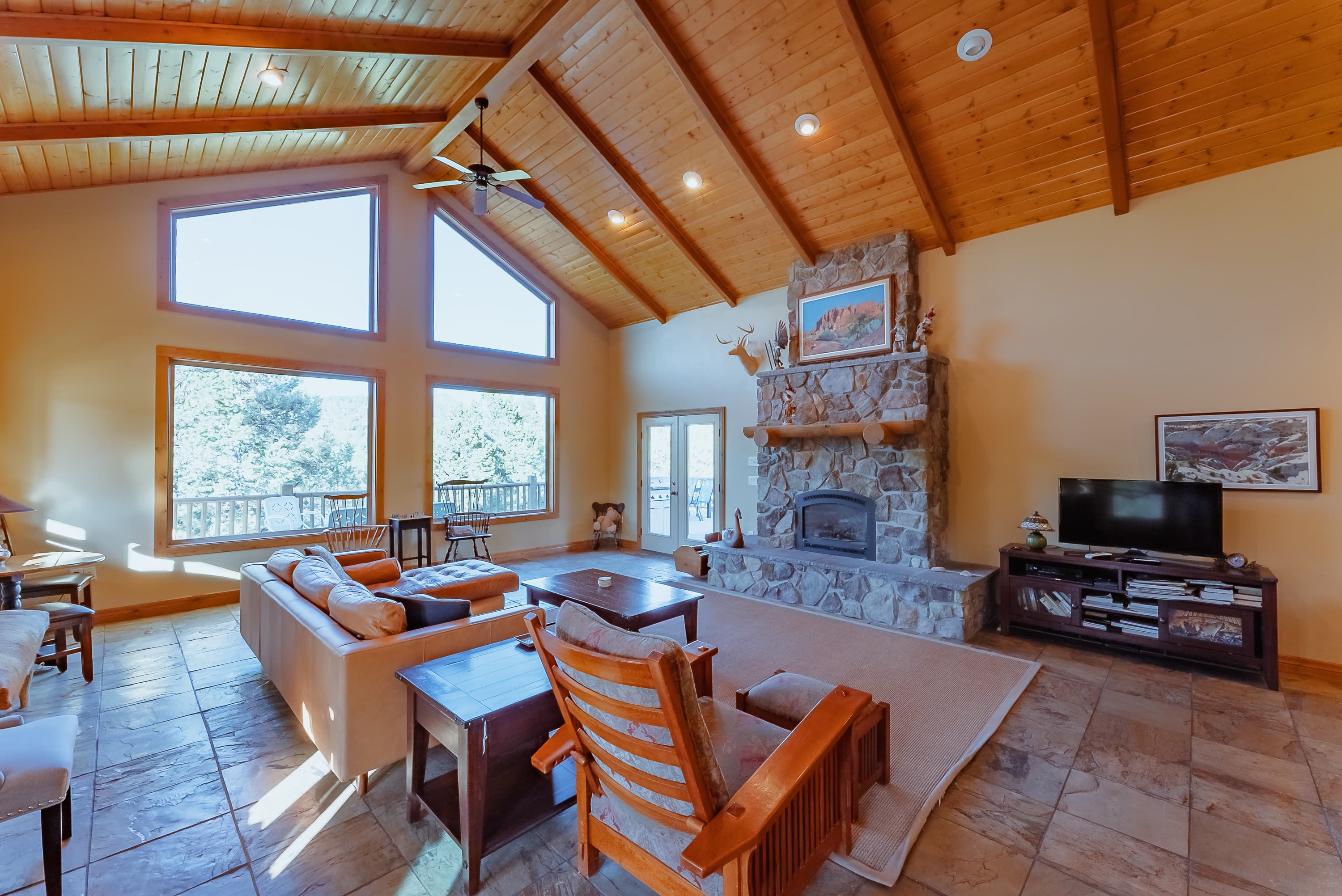 A cozy living room featuring a stone fireplace, large windows, and wooden beams.