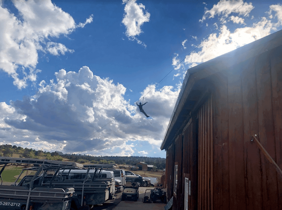 A person zip-lining across the sky with fluffy clouds in the background.