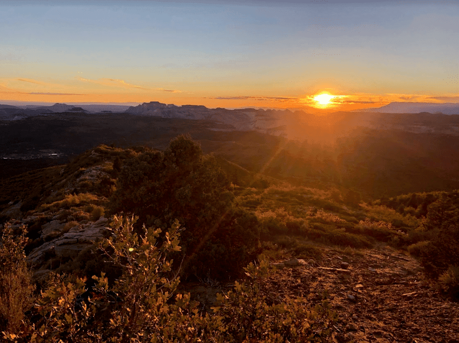 A vibrant sunset casts warm hues over a rugged landscape with distant mountains.