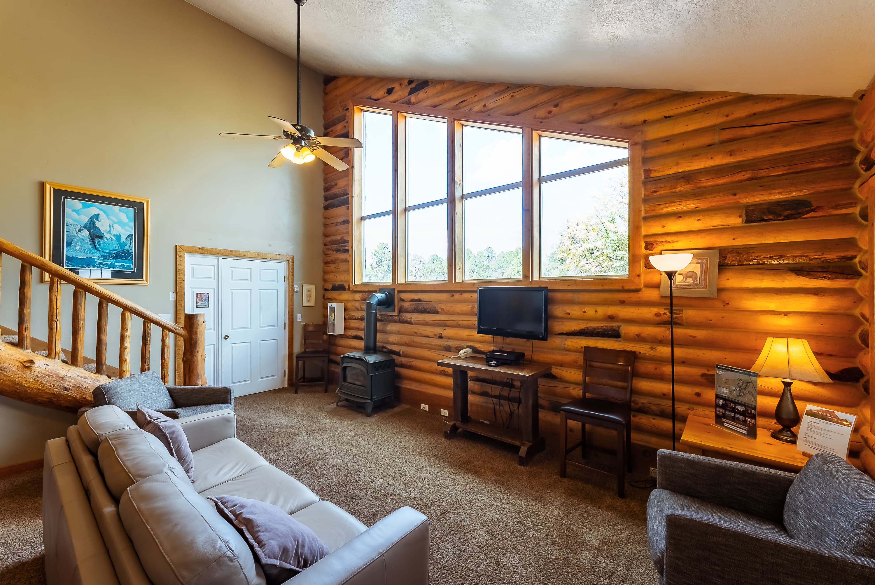 A cozy living room featuring log walls, large windows, a television, and comfortable seating.