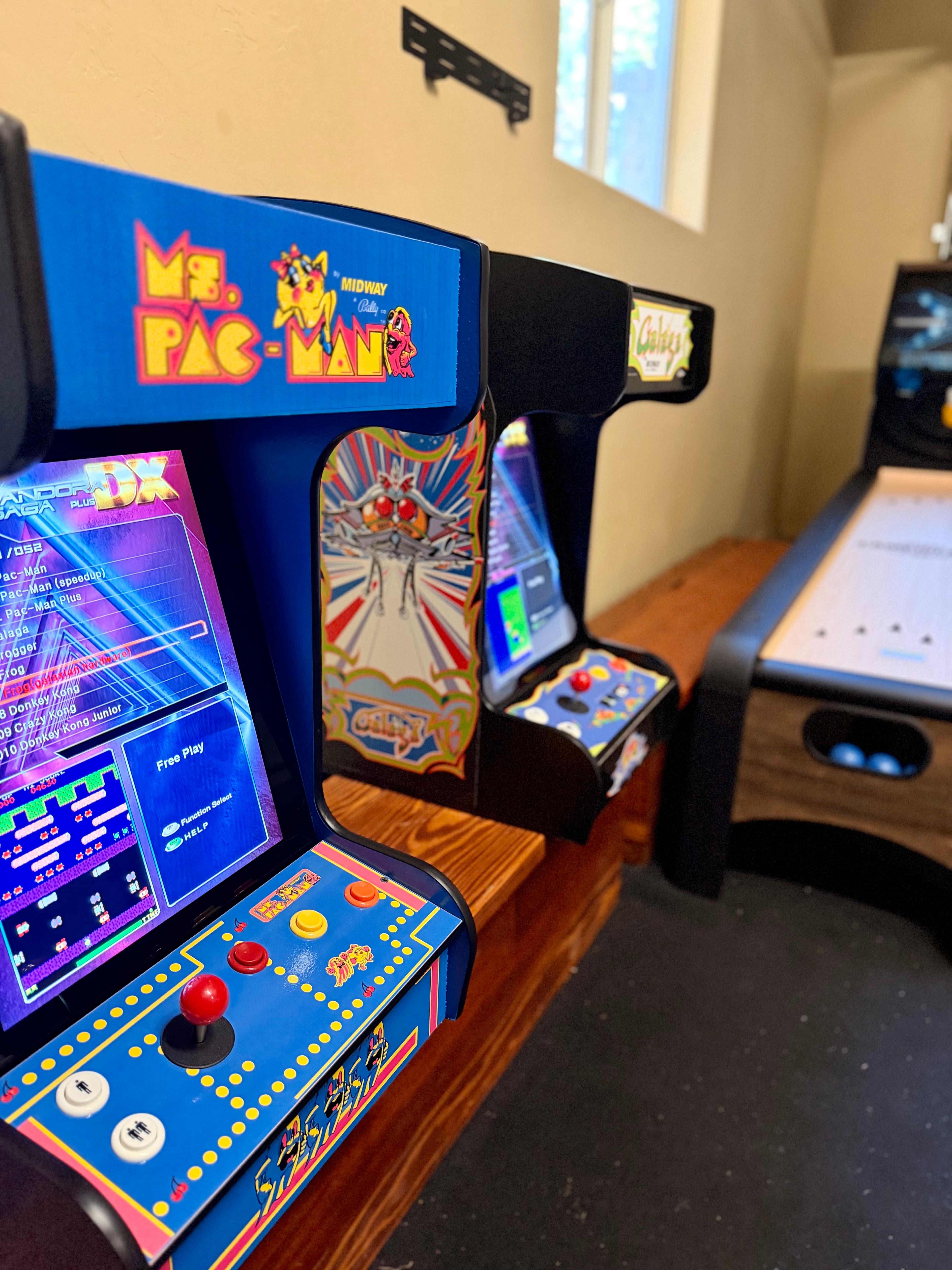 A row of retro arcade game machines, featuring "Ms. Pac-Man" and "Galaga," on a wooden console.