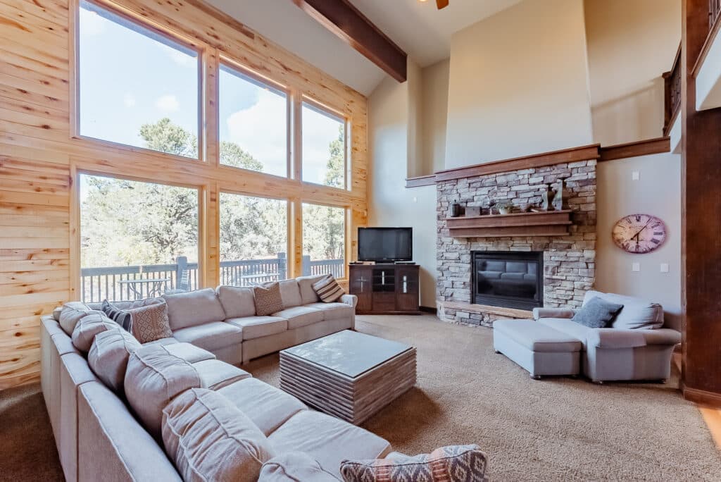 Spacious living room with large windows, a stone fireplace, and modern furnishings.