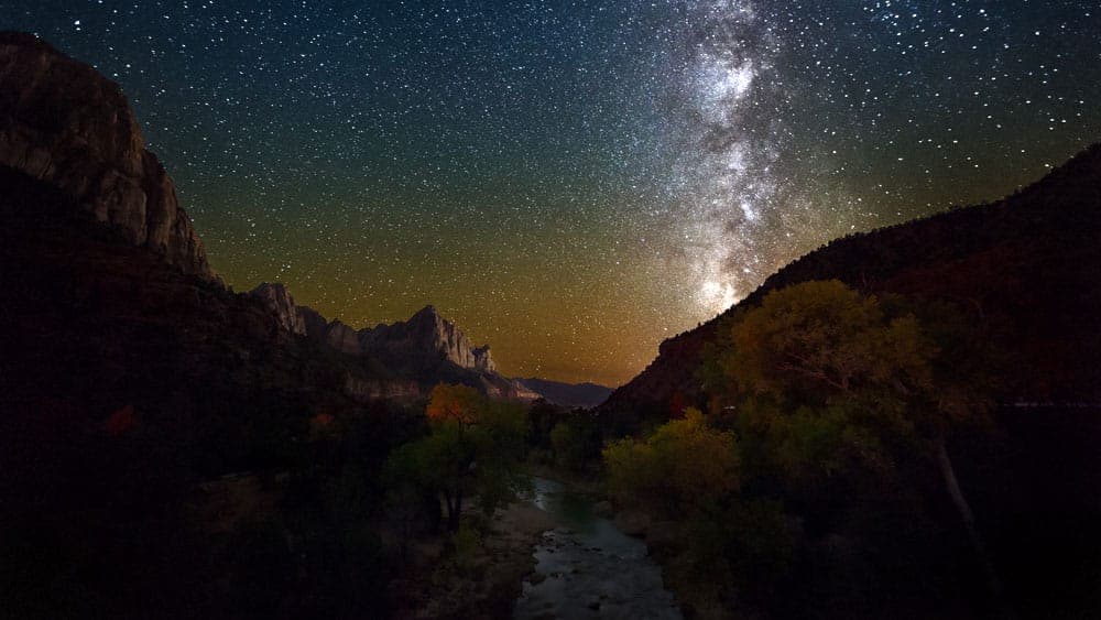 A stunning night sky filled with stars and the Milky Way over a serene mountain landscape and a winding river.