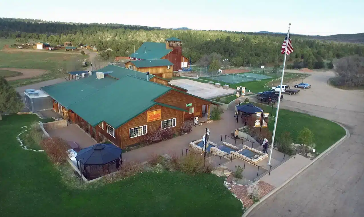Aerial view of a rustic lodge with a green roof, surrounded by trees and a flagpole.