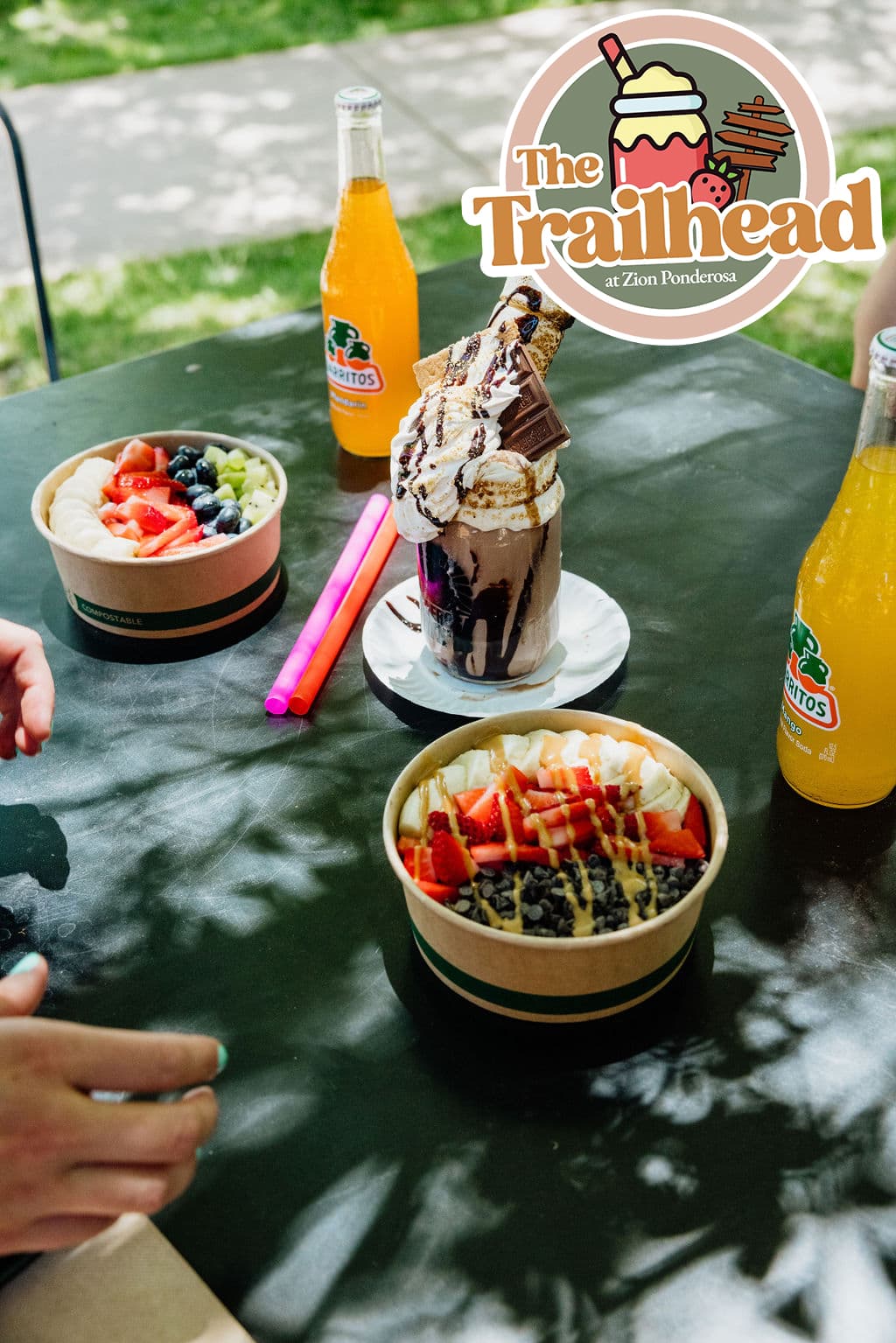 Several colorful desserts and drinks are displayed on a table outdoors.