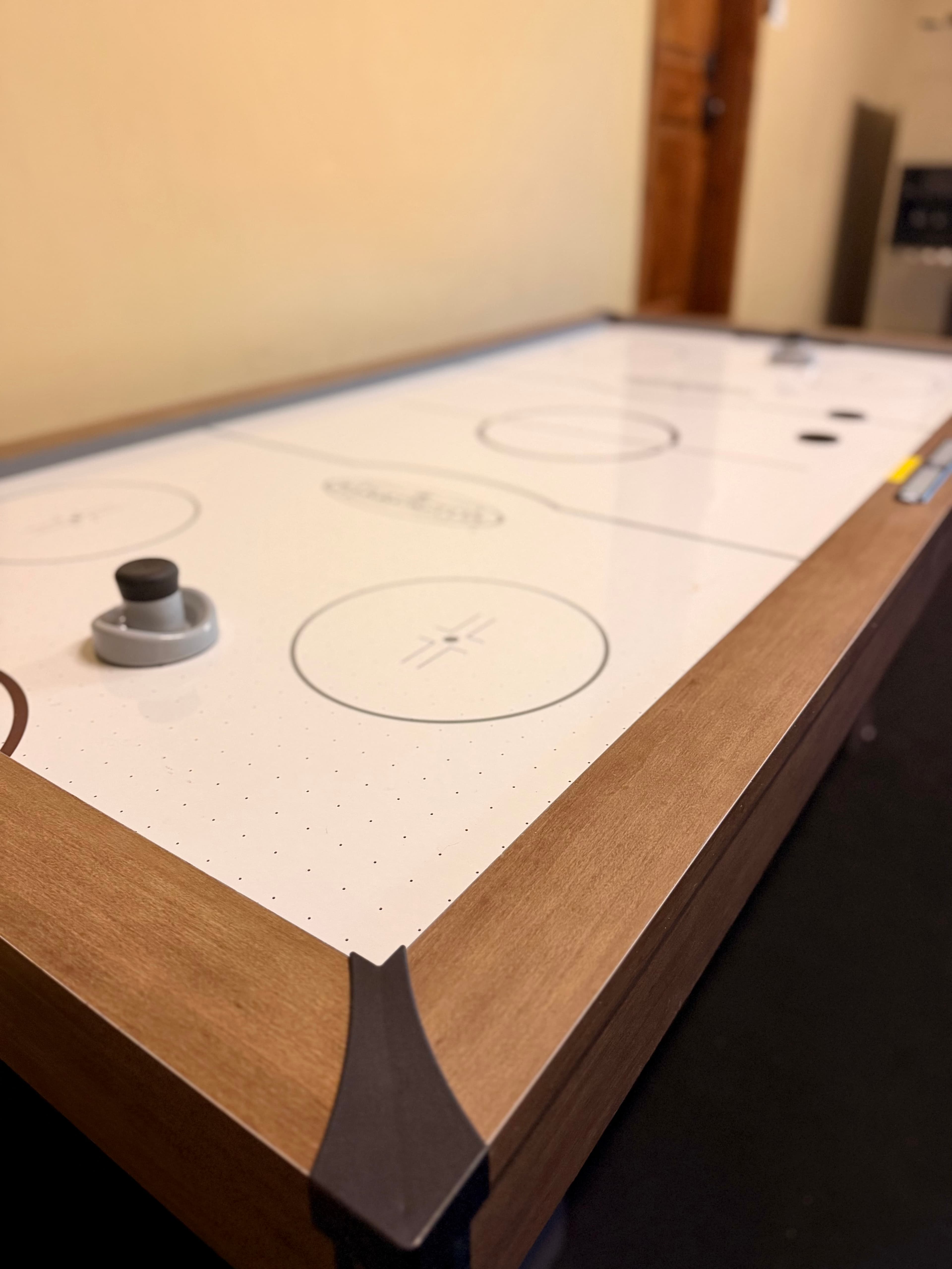 A close-up view of a modern air hockey table with a sleek white surface and wooden edges.