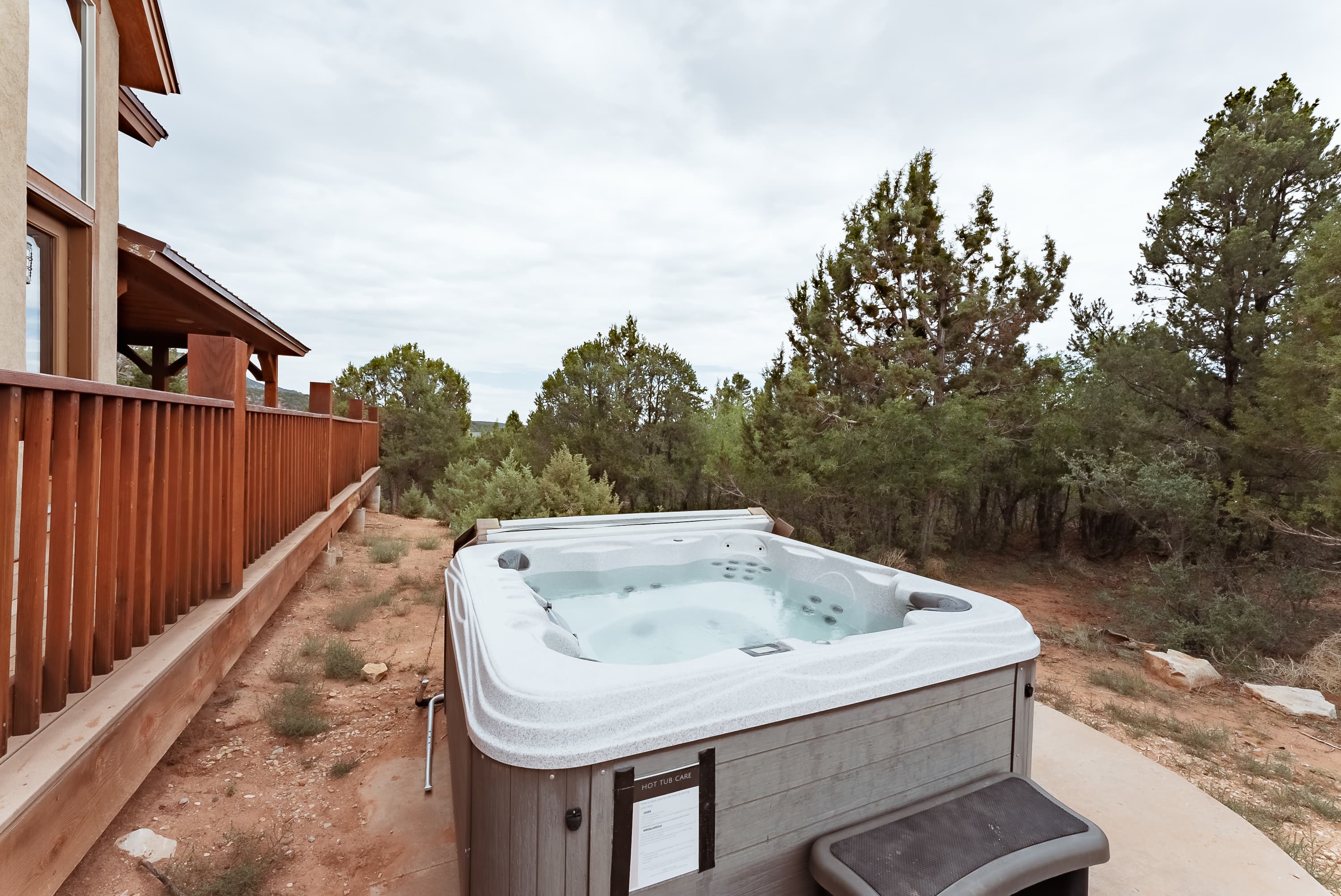 A hot tub is situated outdoors next to a wooden deck, surrounded by trees.
