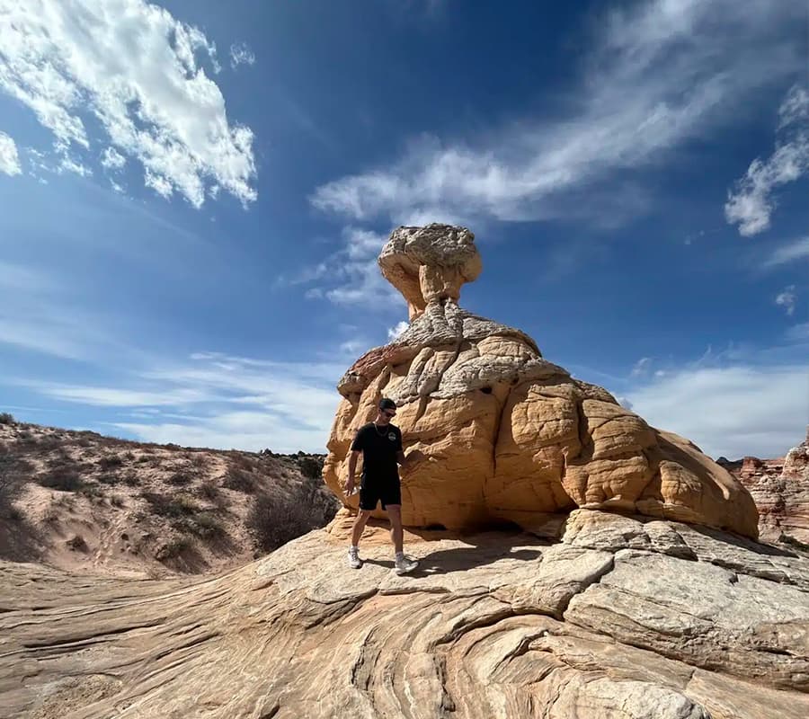 A person stands near a uniquely shaped rock formation under a blue sky with scattered clouds.