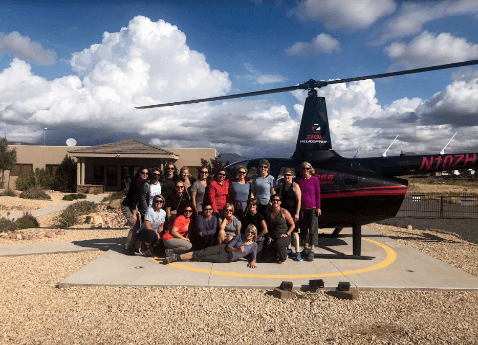 A group of people poses together in front of a helicopter on a sunny day.