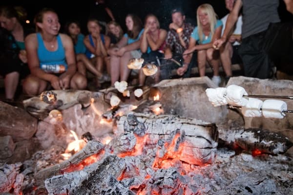 A group of people gather around a campfire, roasting marshmallows.