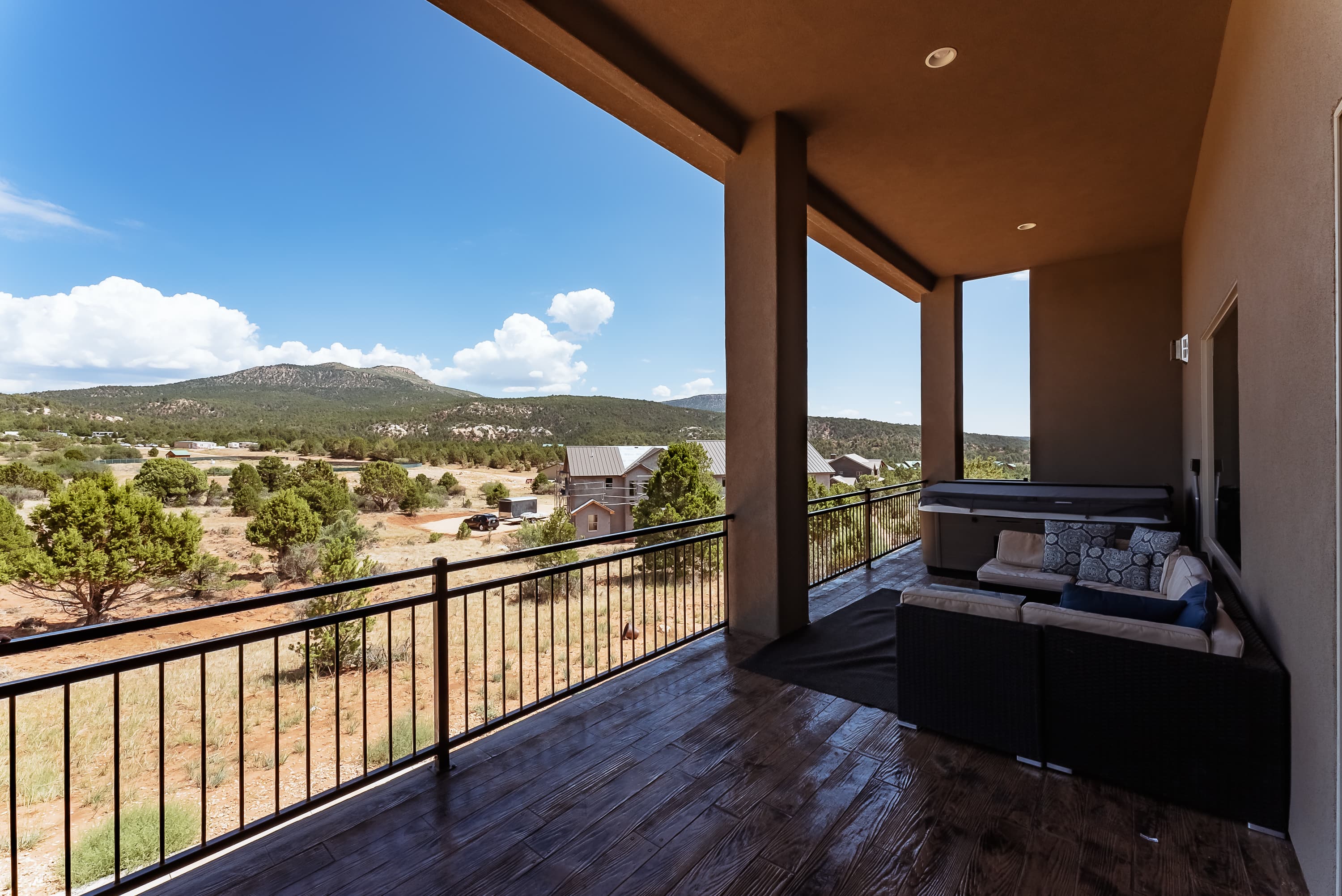 A patio with a couch overlooks a scenic landscape of mountains and greenery under a cloudy blue sky.