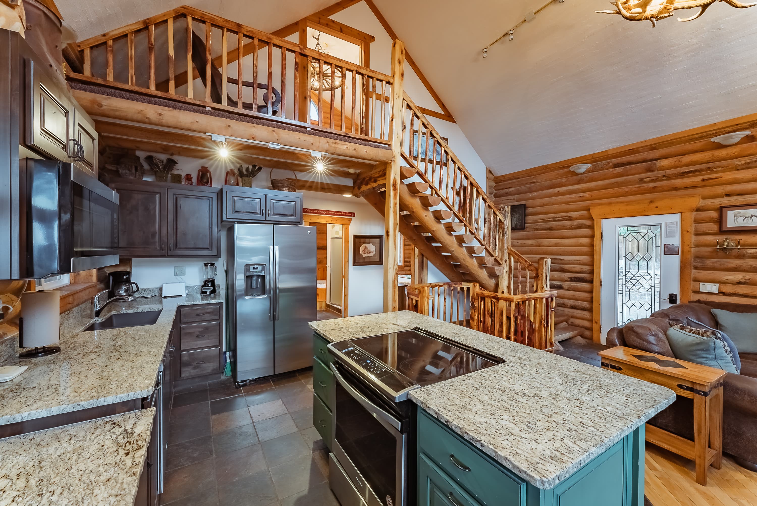 A modern log cabin kitchen with a central island, stainless steel appliances, and a staircase leading to an upper level.