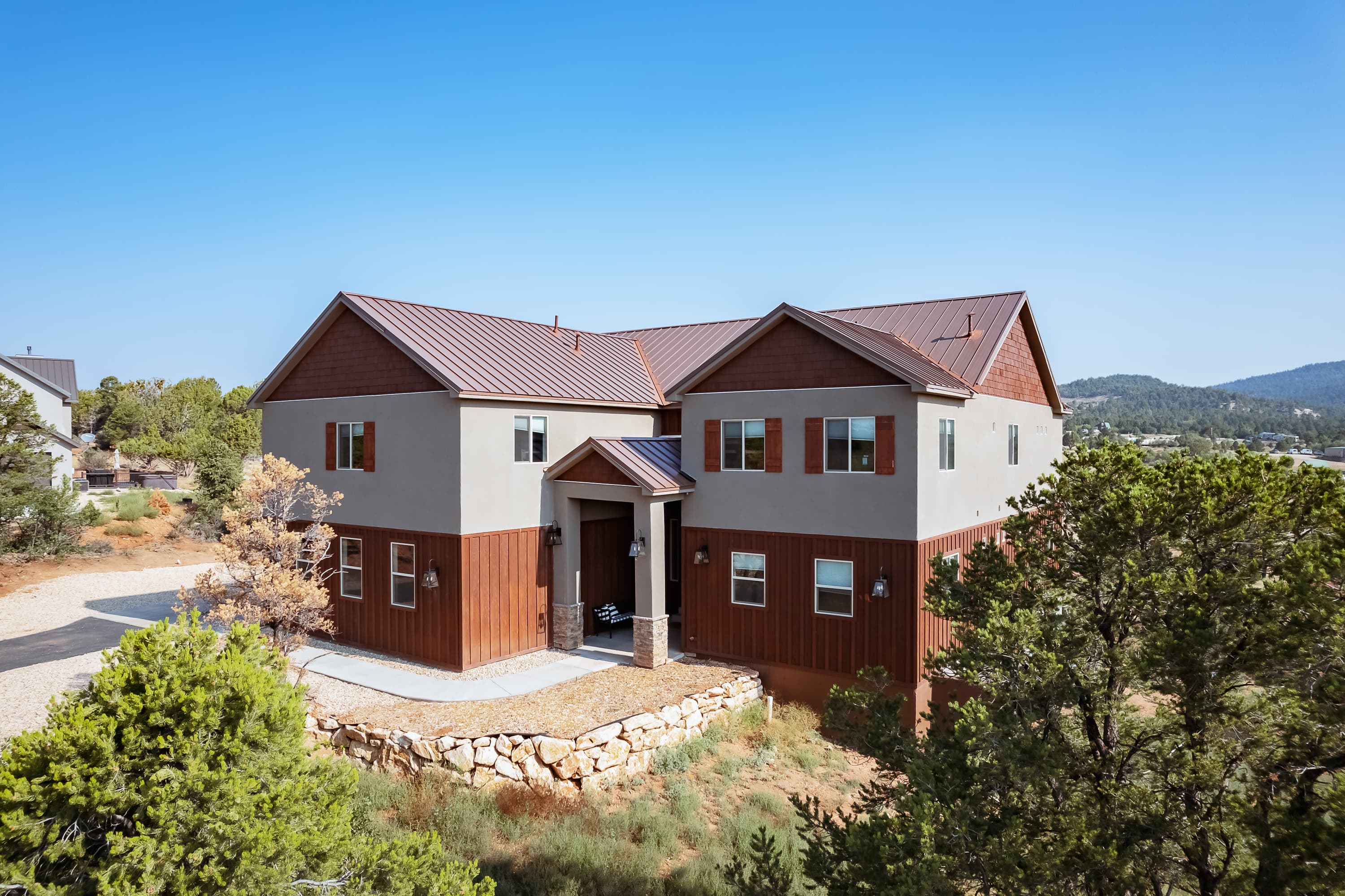 A modern two-story house with a metal roof and a mix of gray and wood paneling, set in a natural landscape.