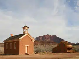 Two historic brick buildings with a mountain backdrop under a cloudy sky.