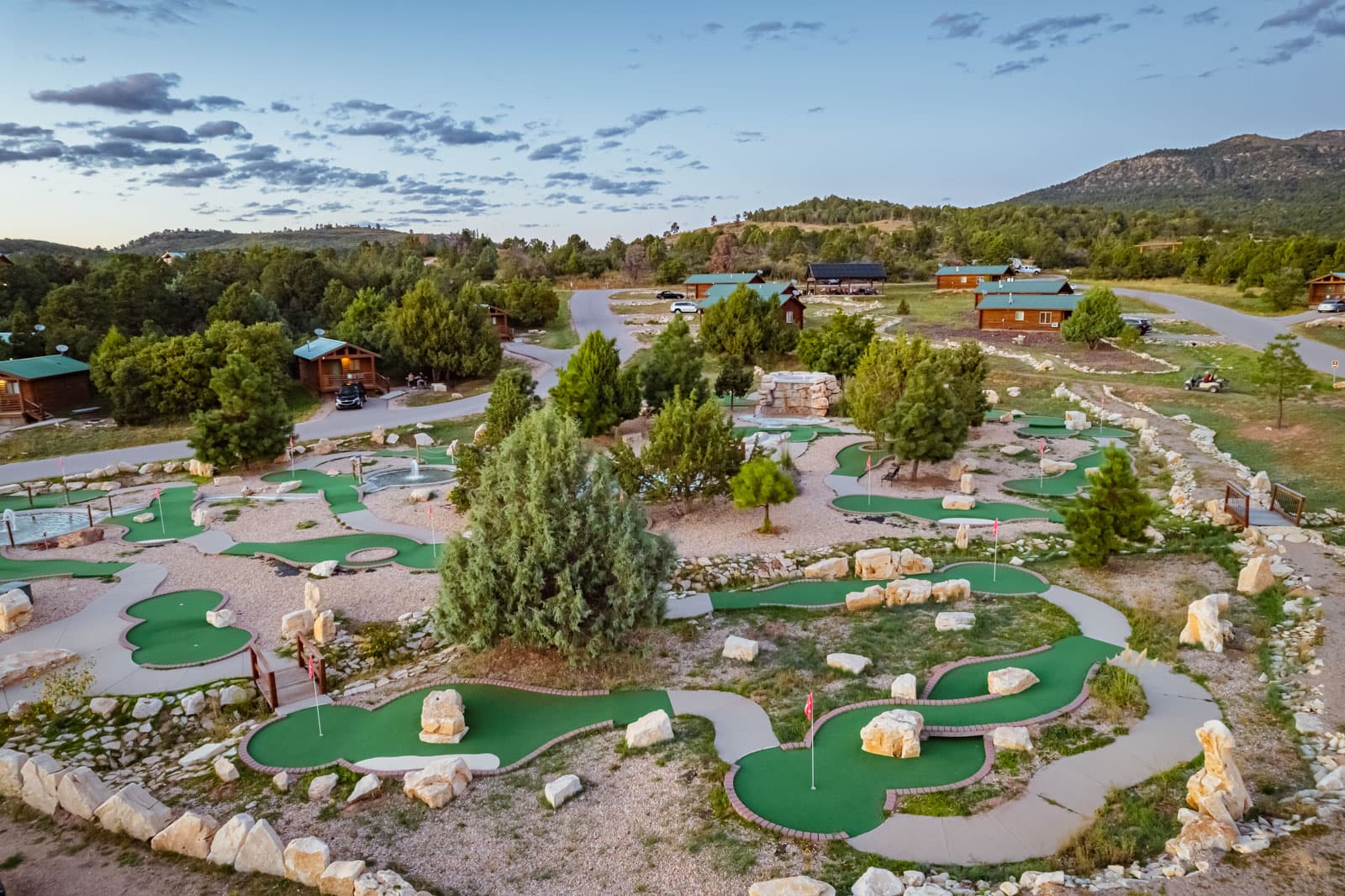 Aerial view of a mini-golf course surrounded by greenery and cabins under a cloudy sky.