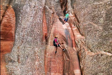 Two climbers navigate a narrow rock crevice in a rugged landscape.