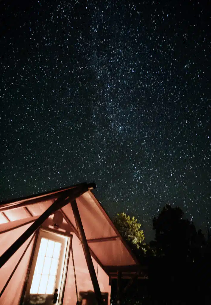 A cabin illuminated at night under a star-filled sky.