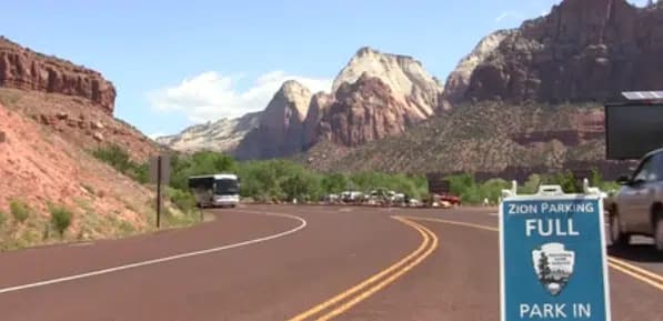 A road sign indicating "Zion Parking Full" alongside a scenic highway and mountains.