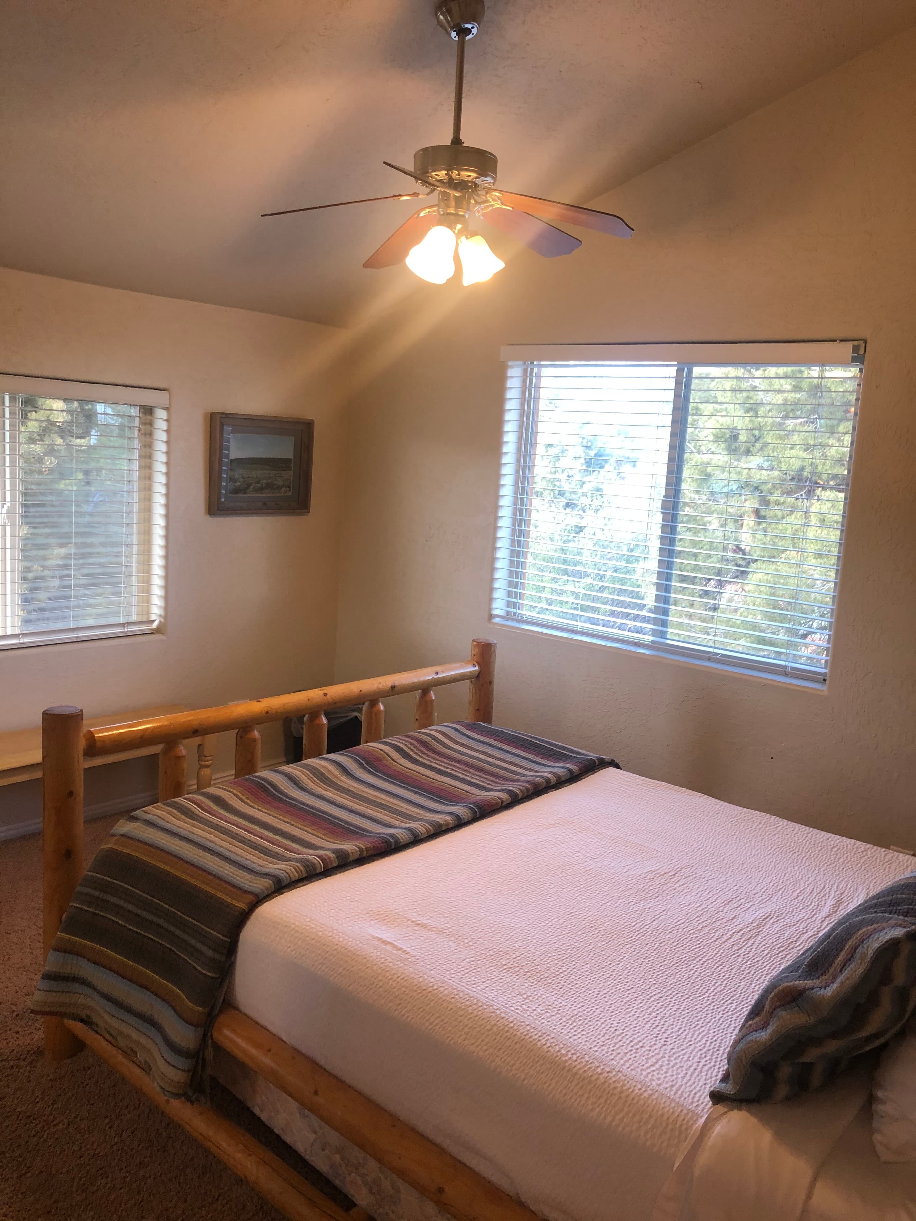 A cozy bedroom featuring a wooden bed, striped blanket, and large windows with natural light.