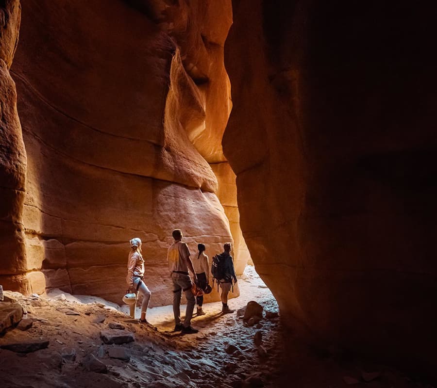 Four people exploring a narrow, illuminated canyon.