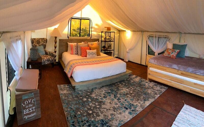 A stylish glamping tent interior featuring a queen bed, twin bed, cozy seating area, and decorative accents.