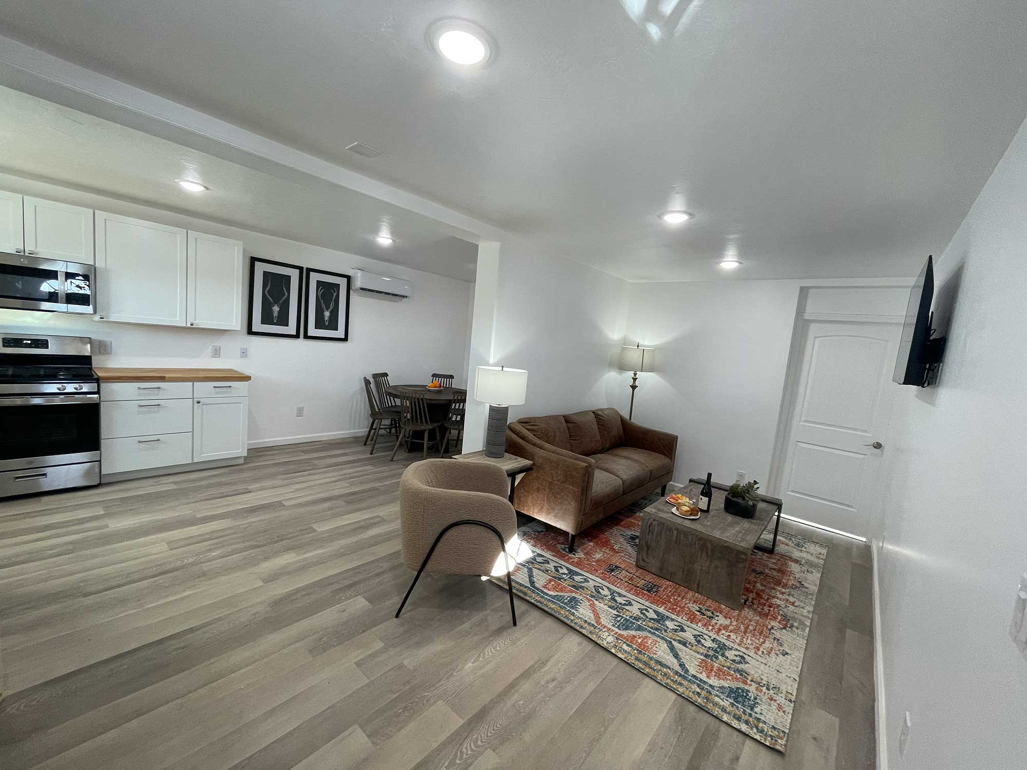 A modern living area with a brown leather sofa, a coffee table, and a dining set, featuring light hardwood flooring and white walls.