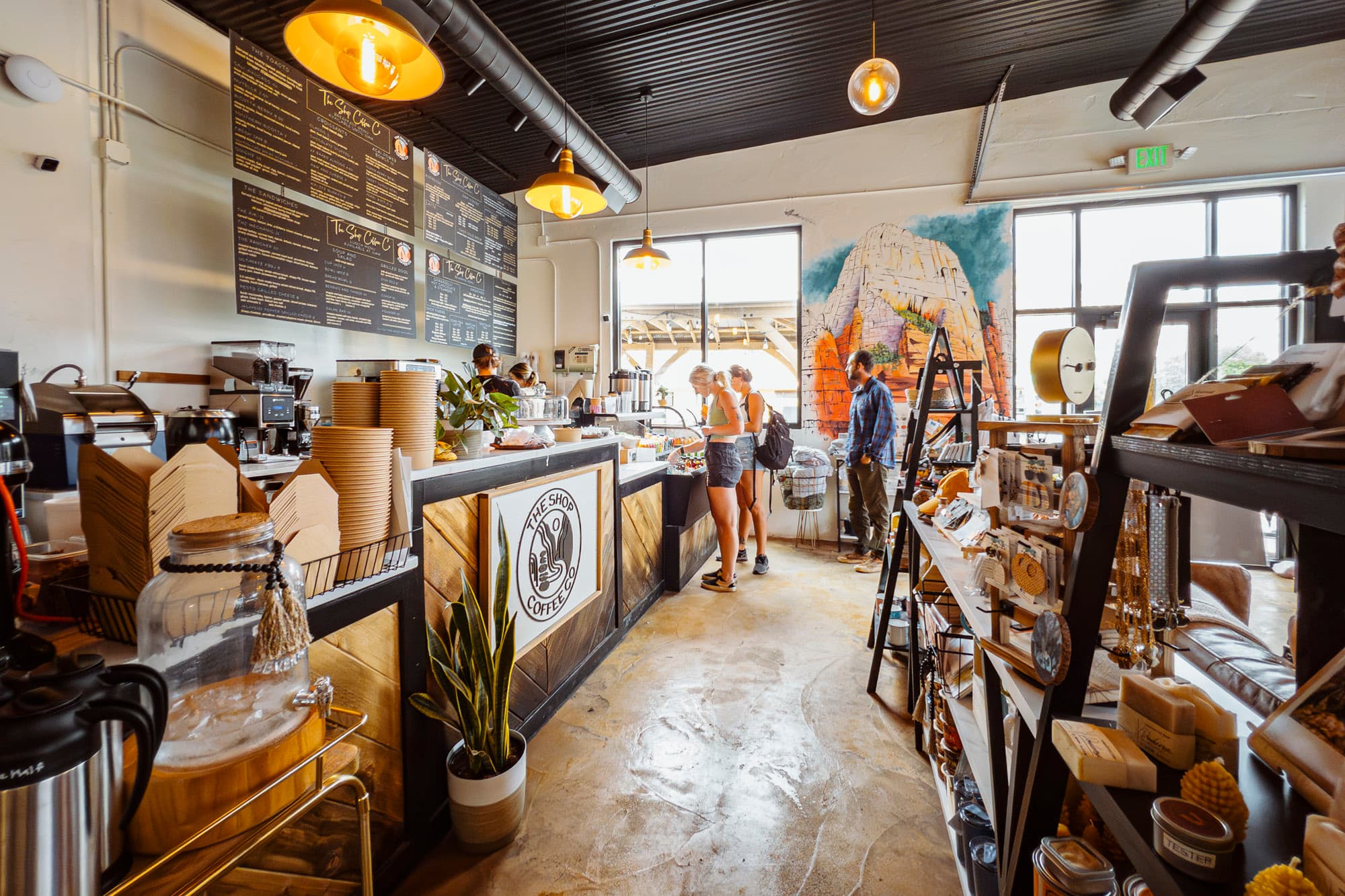 A vibrant coffee shop interior with a menu board, customers ordering, and shelves filled with merchandise.