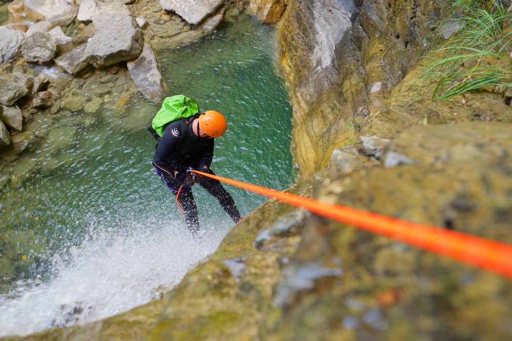 A climber rappels down a rocky cliff beside a turquoise pool of water.