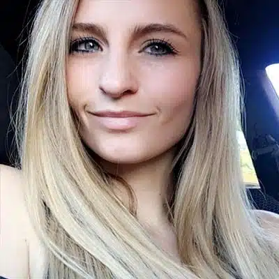 A woman with long blonde hair smiles in a car.