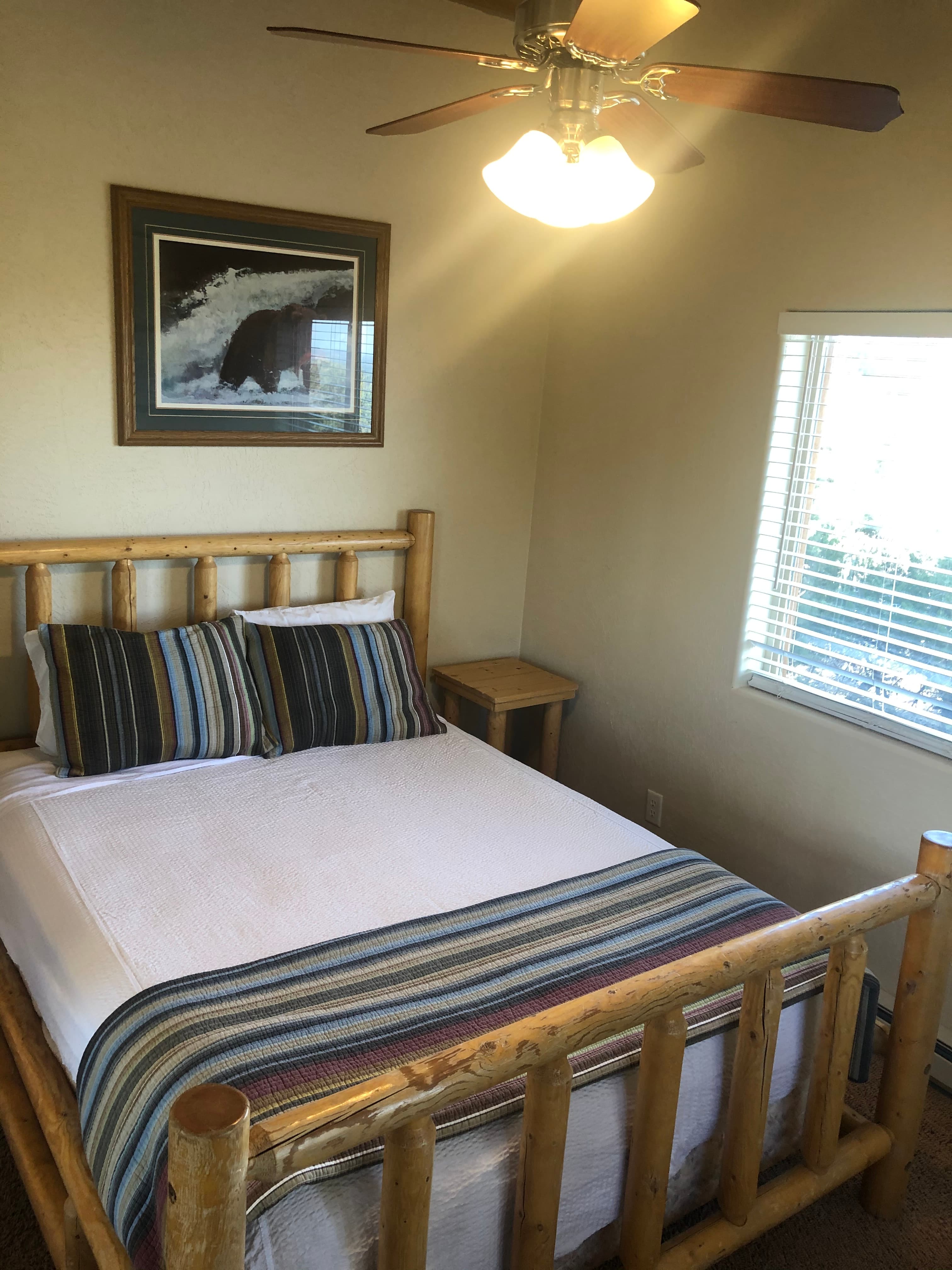 A cozy bedroom featuring a wooden bed with striped bedding, a bedside table, and a painted wall decor.