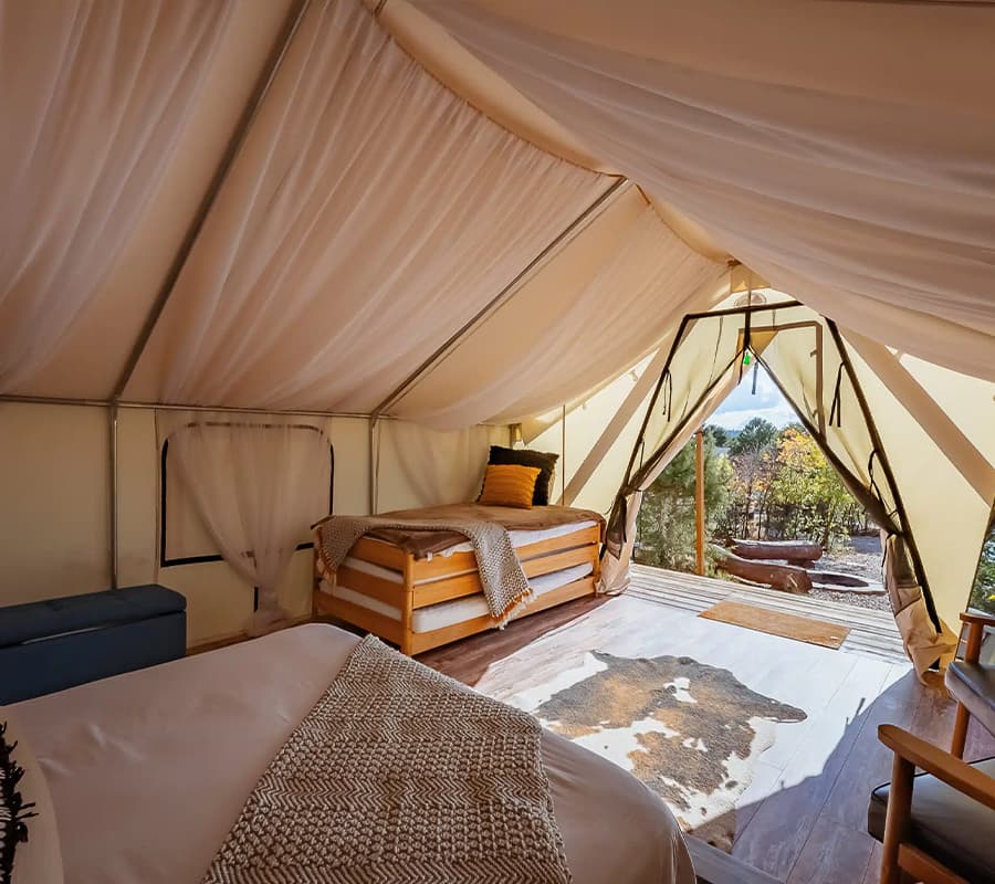 Interior of a cozy canvas tent featuring a bed, a wooden frame, and a view of nature through an open doorway.