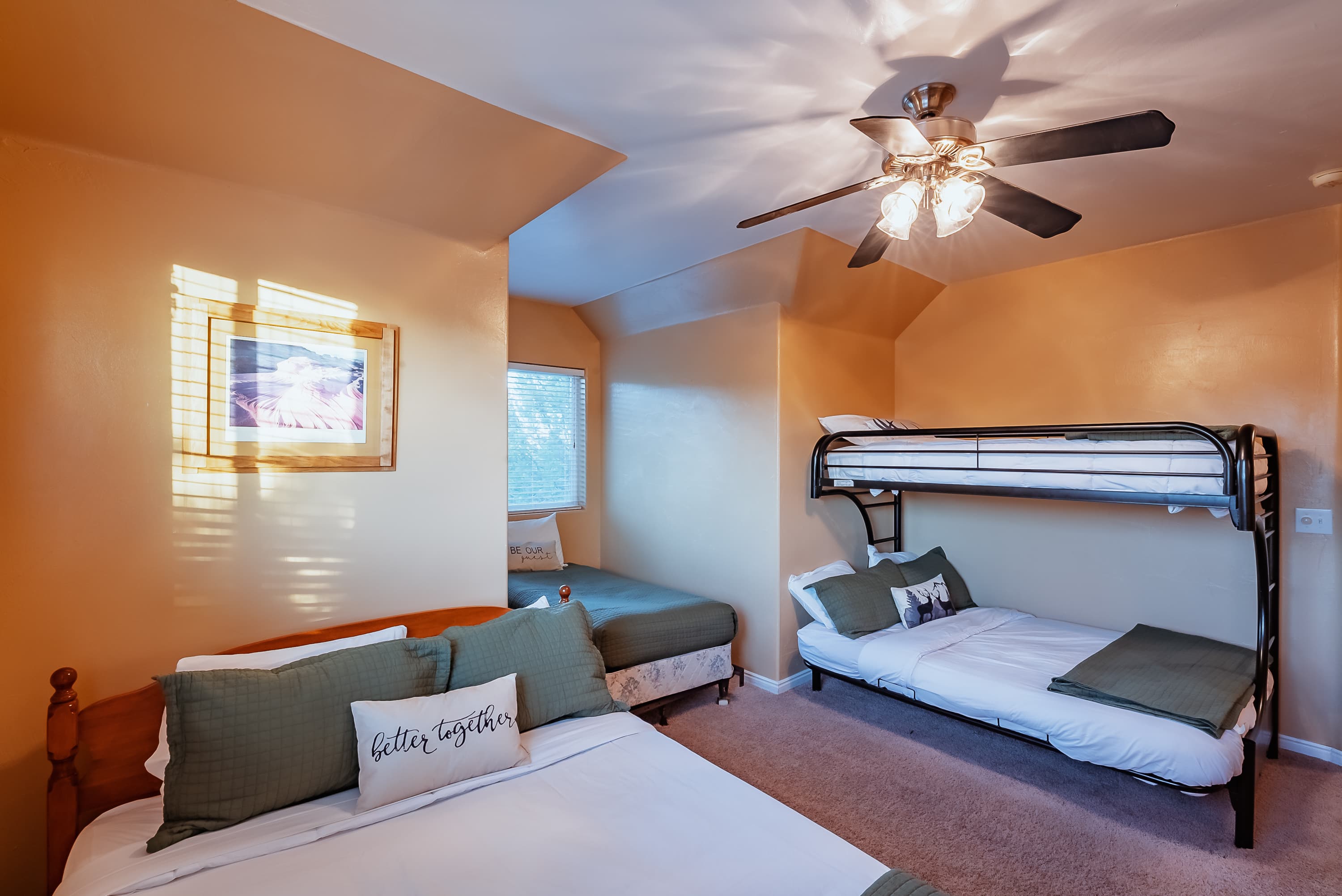 A cozy bedroom with a ceiling fan, featuring a queen bed, a bunk bed, and a twin bed with neutral decor.