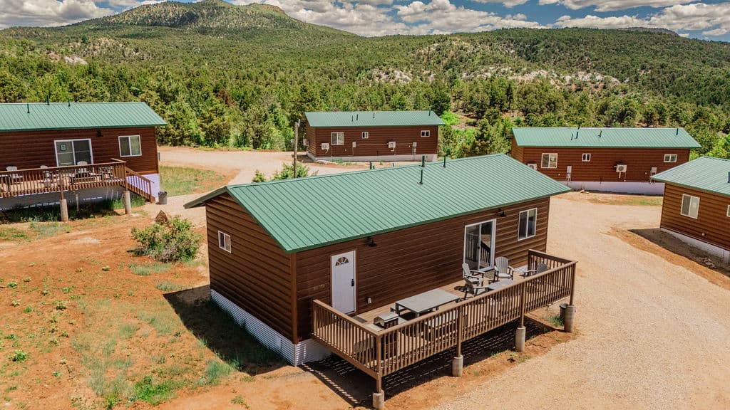 Aerial view of several cabins with green roofs surrounded by trees and mountains.