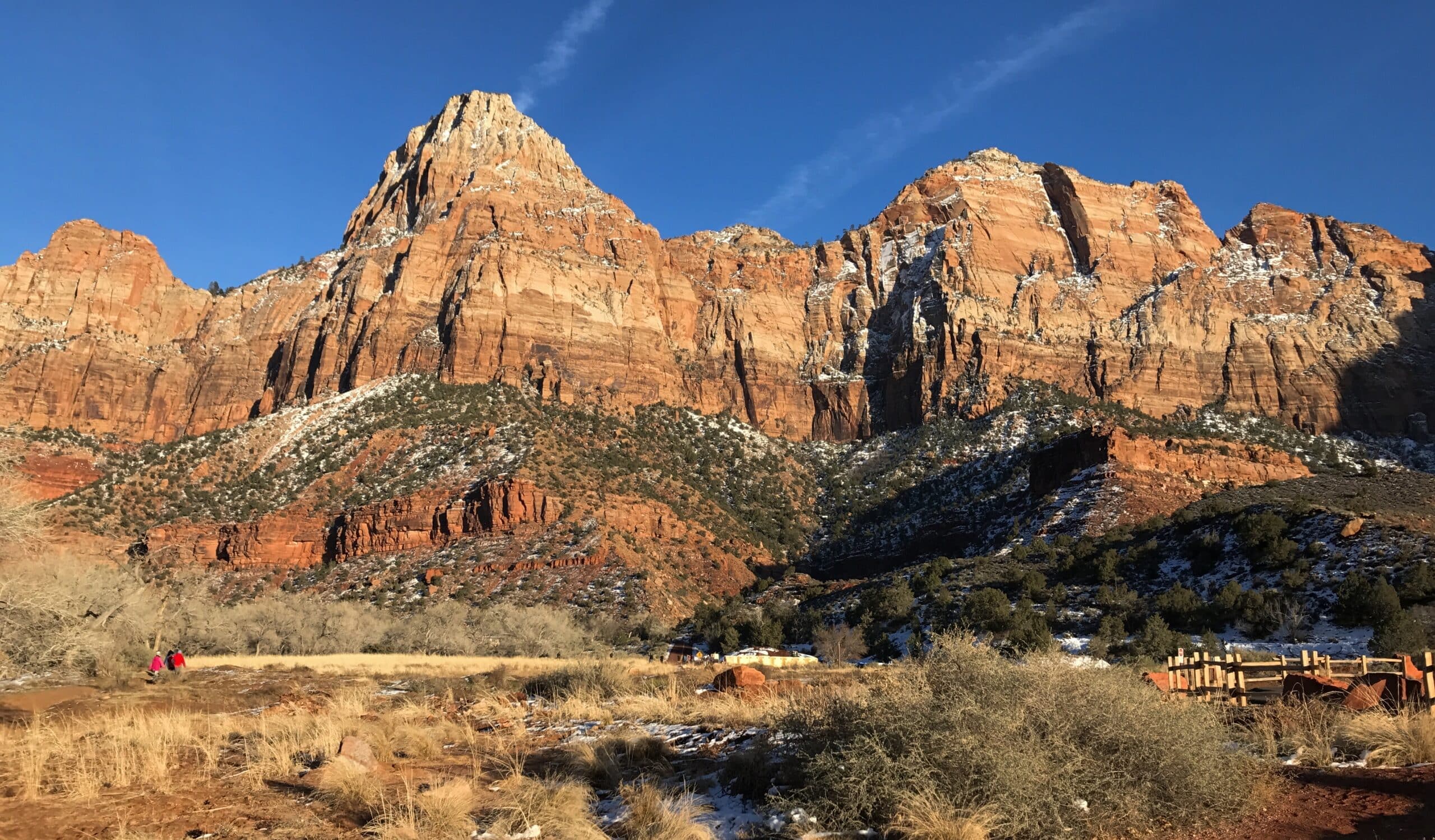 Sunlit cliffs rise majestically over a snowy landscape in Zion National Park.
