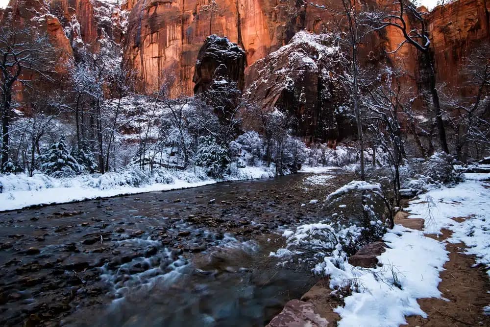 A snowy river winds through a canyon landscape with towering red rock formations.