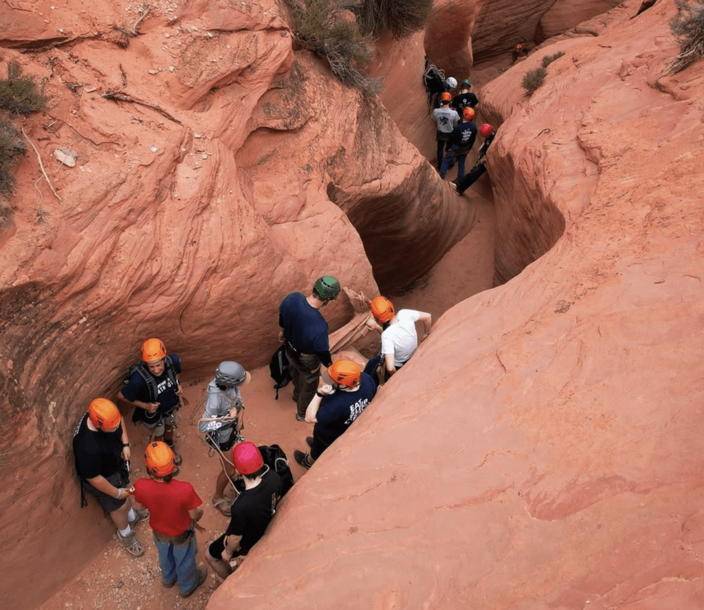 A group of people in helmets prepares for an outdoor activity in a red rock canyon.