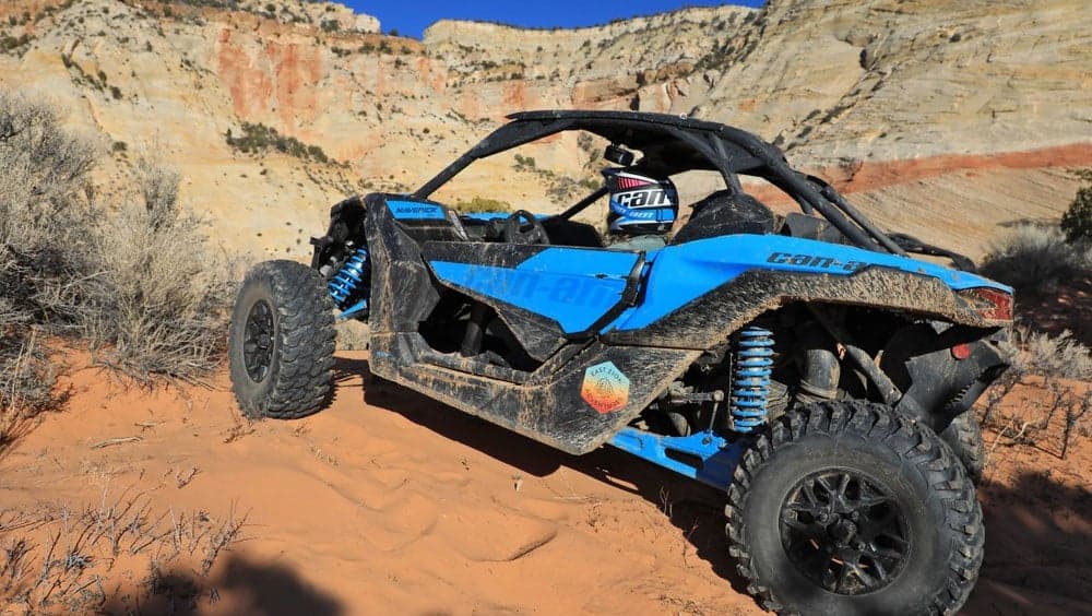 A blue off-road vehicle parked on sandy terrain with rocky cliffs in the background.